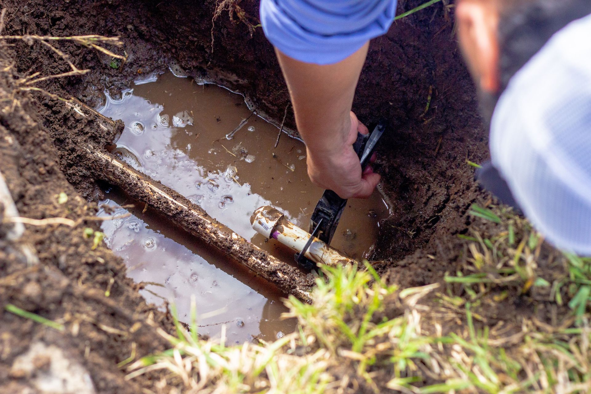 A person is fixing a broken pipe in the dirt.