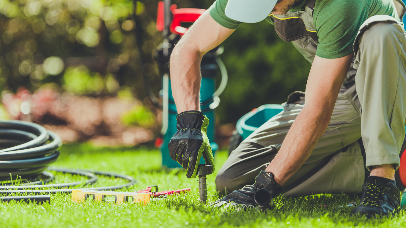 A man is kneeling down in the grass working on a sprinkler system.