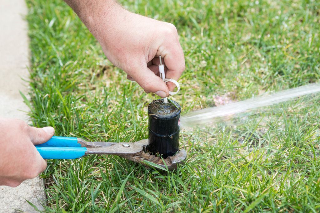 A person is fixing a lawn sprinkler with a pair of pliers.