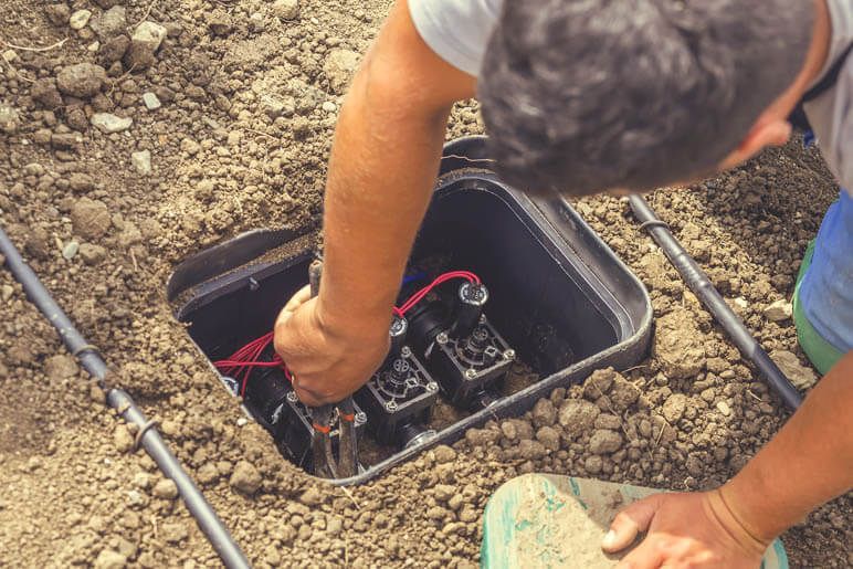 A man is working on a sprinkler system in the dirt.