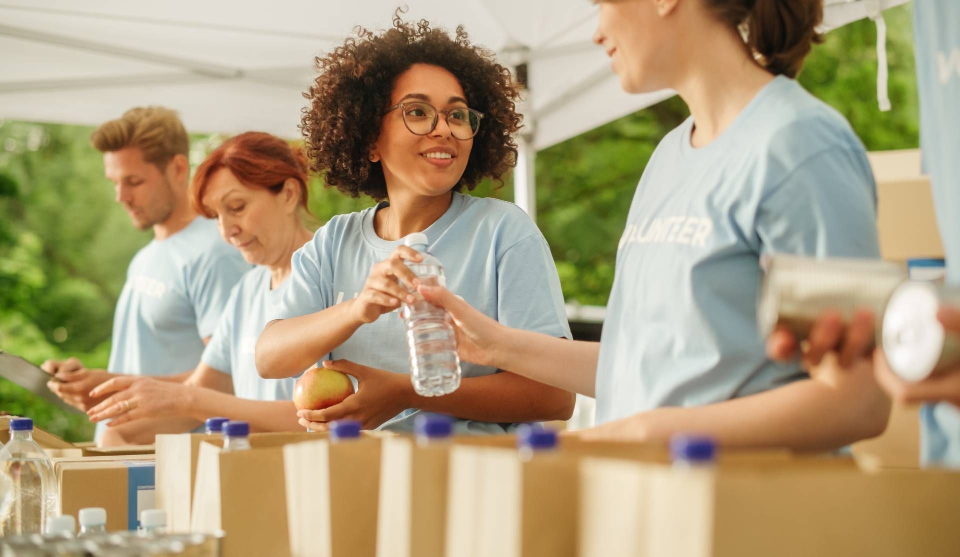 Volunteers sorting canned goods at a donation table under a white canopy