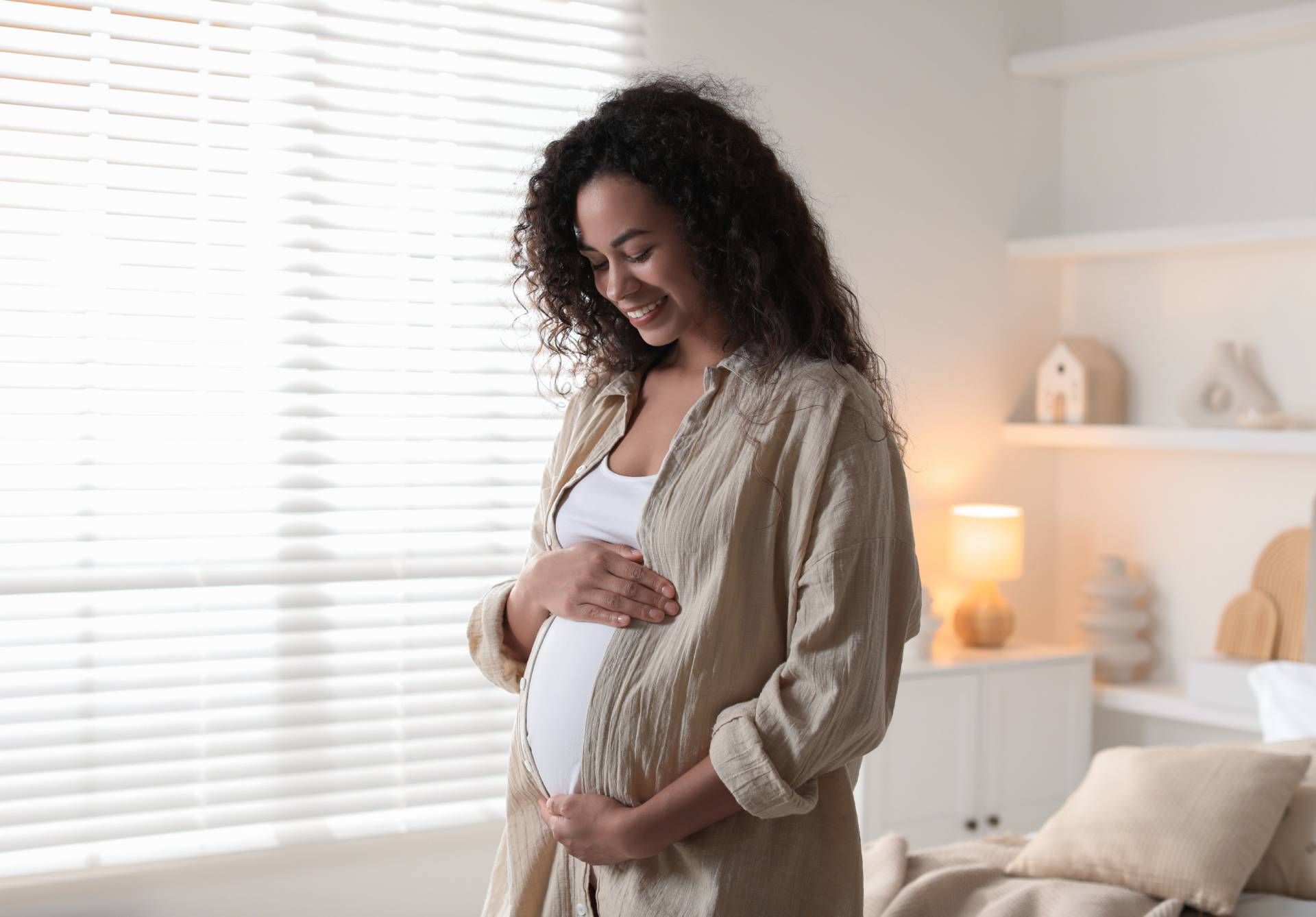 Pregnant woman smiling and holding her belly in a bright bedroom