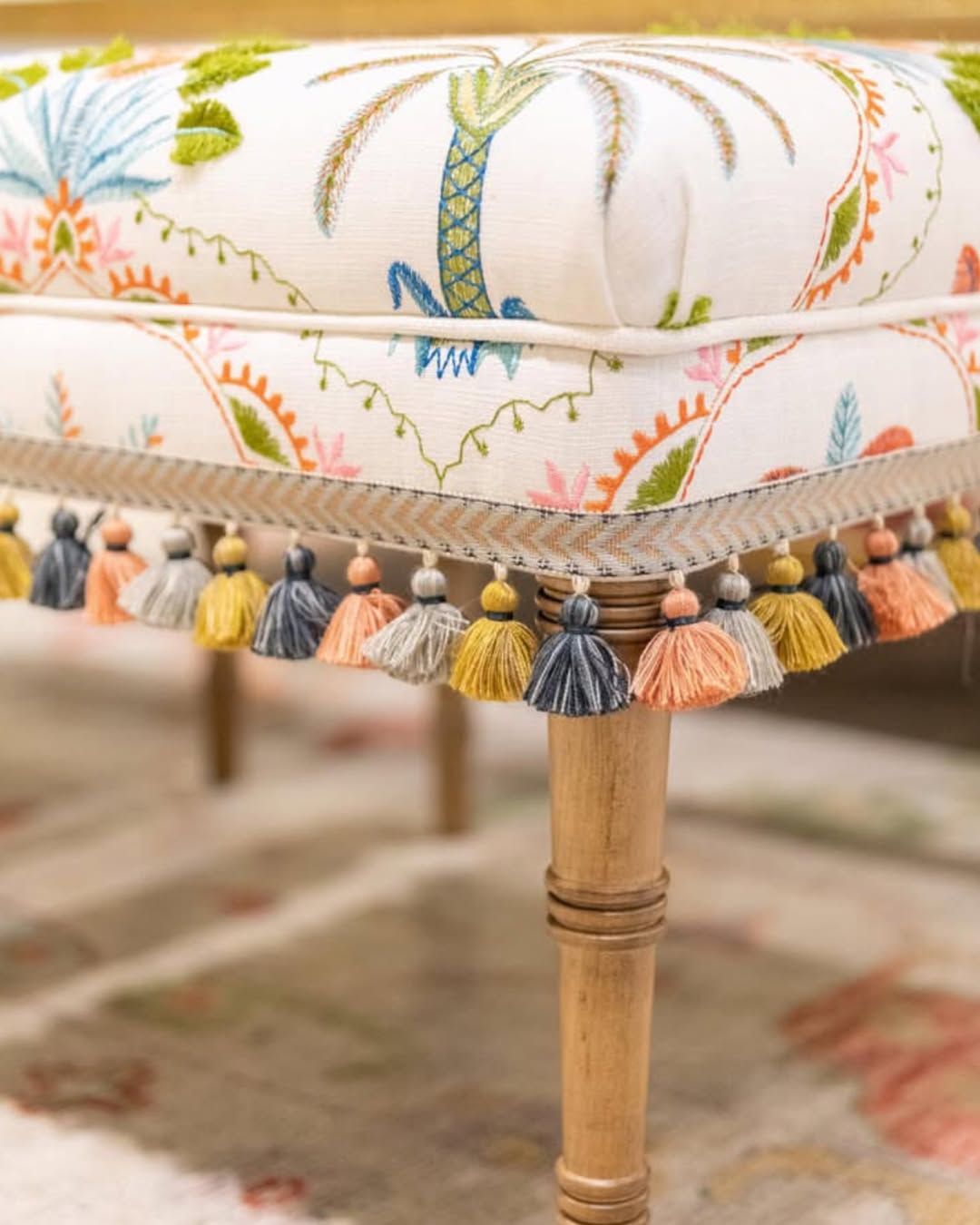 A chair with a floral pattern and tassels on the legs.