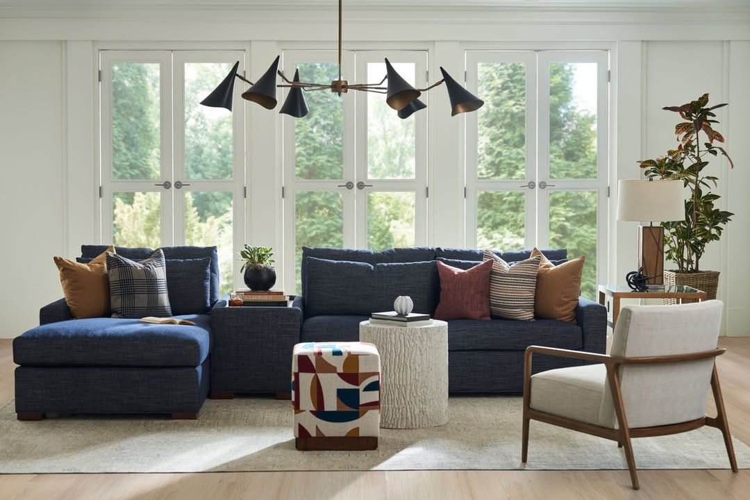 A living room with a couch , chair , ottoman , and table.
