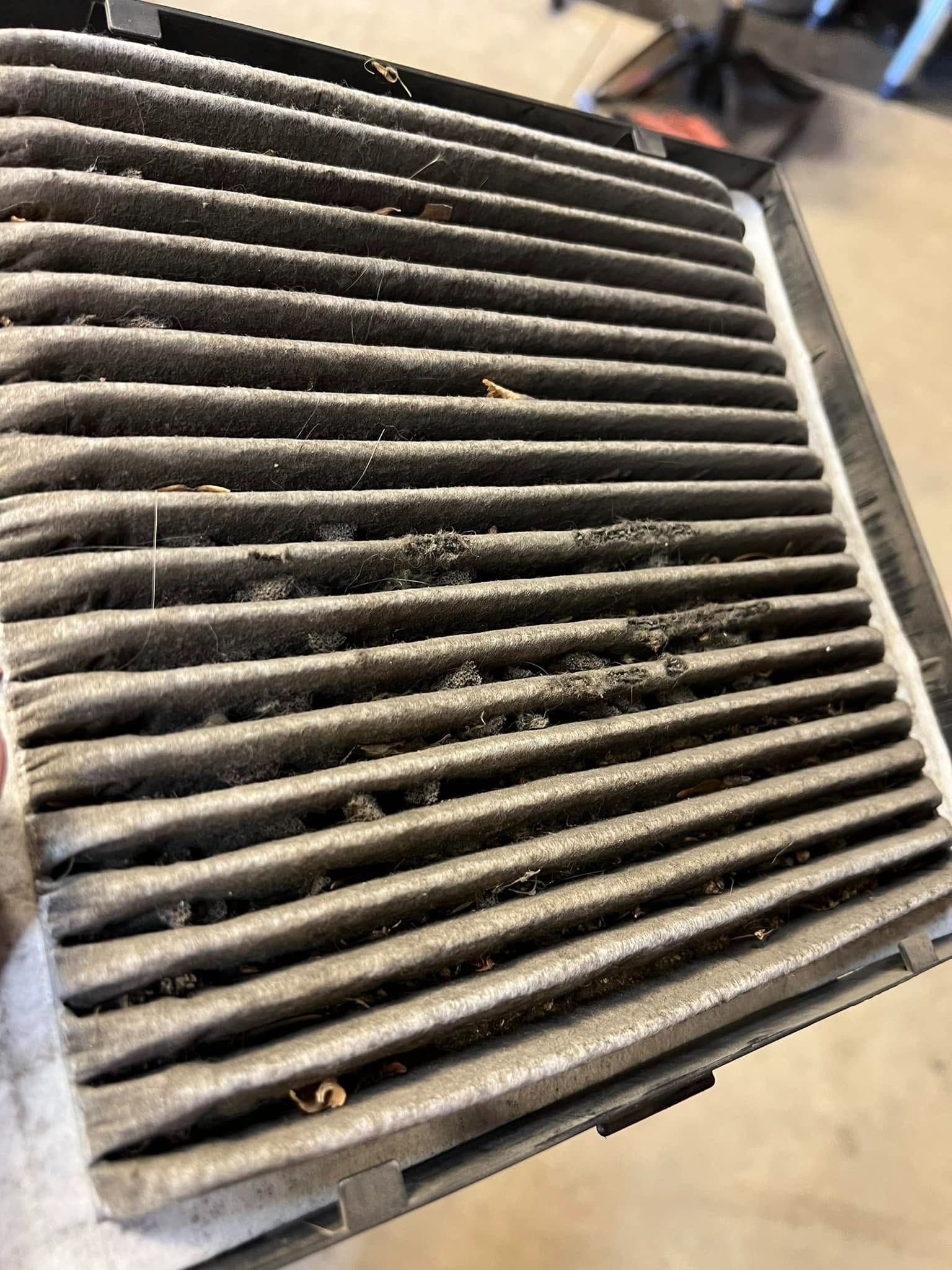 Dirty pleated air filter with gray dust buildup, shown in a close-up.