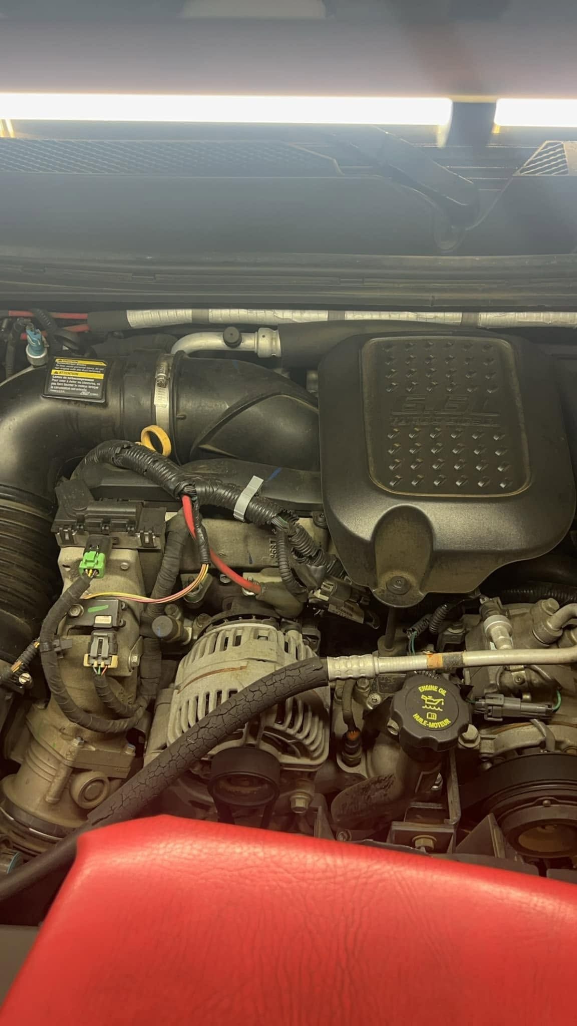 Close-up of a car engine bay with hoses, wiring, and a black engine cover under the hood.