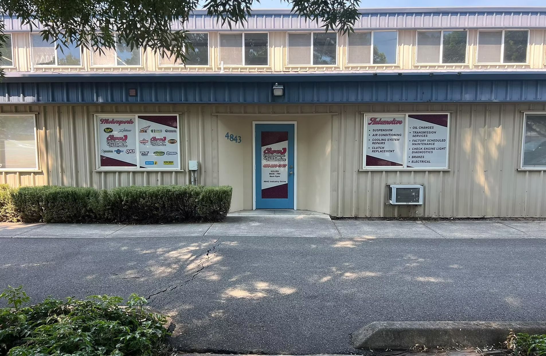Small beige storefront with blue door, menu signs, and gravel parking area under trees