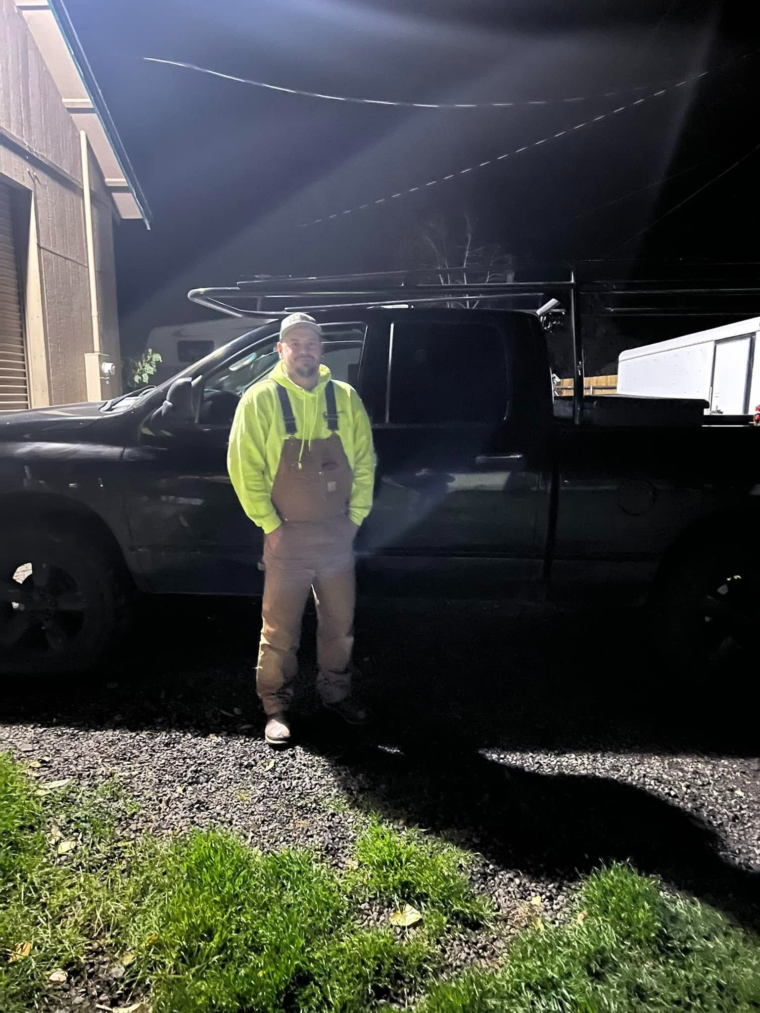 Person in a neon jacket standing beside a black pickup truck at night under bright lights.