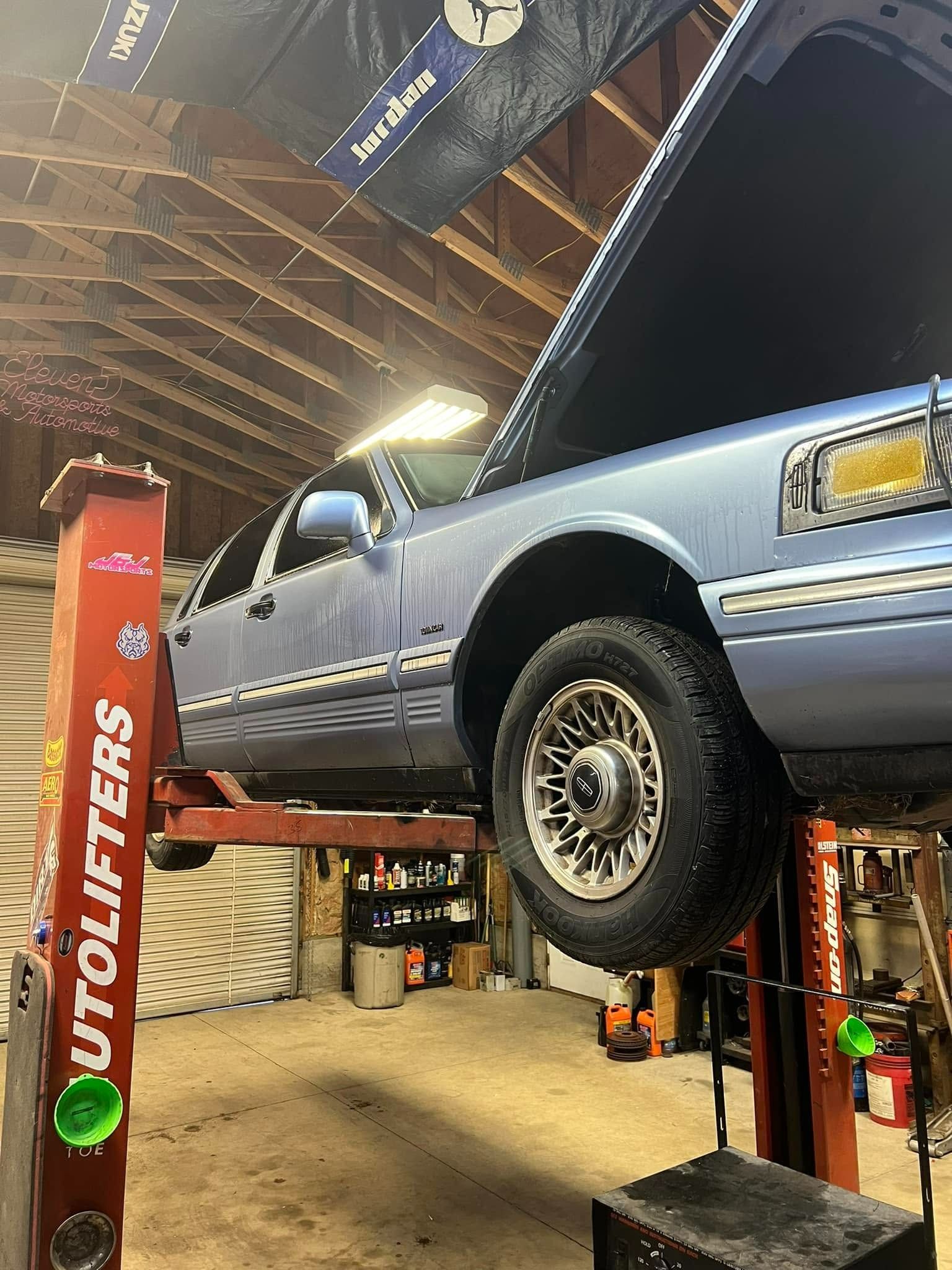 Light blue pickup truck raised on a lift inside an auto repair shop