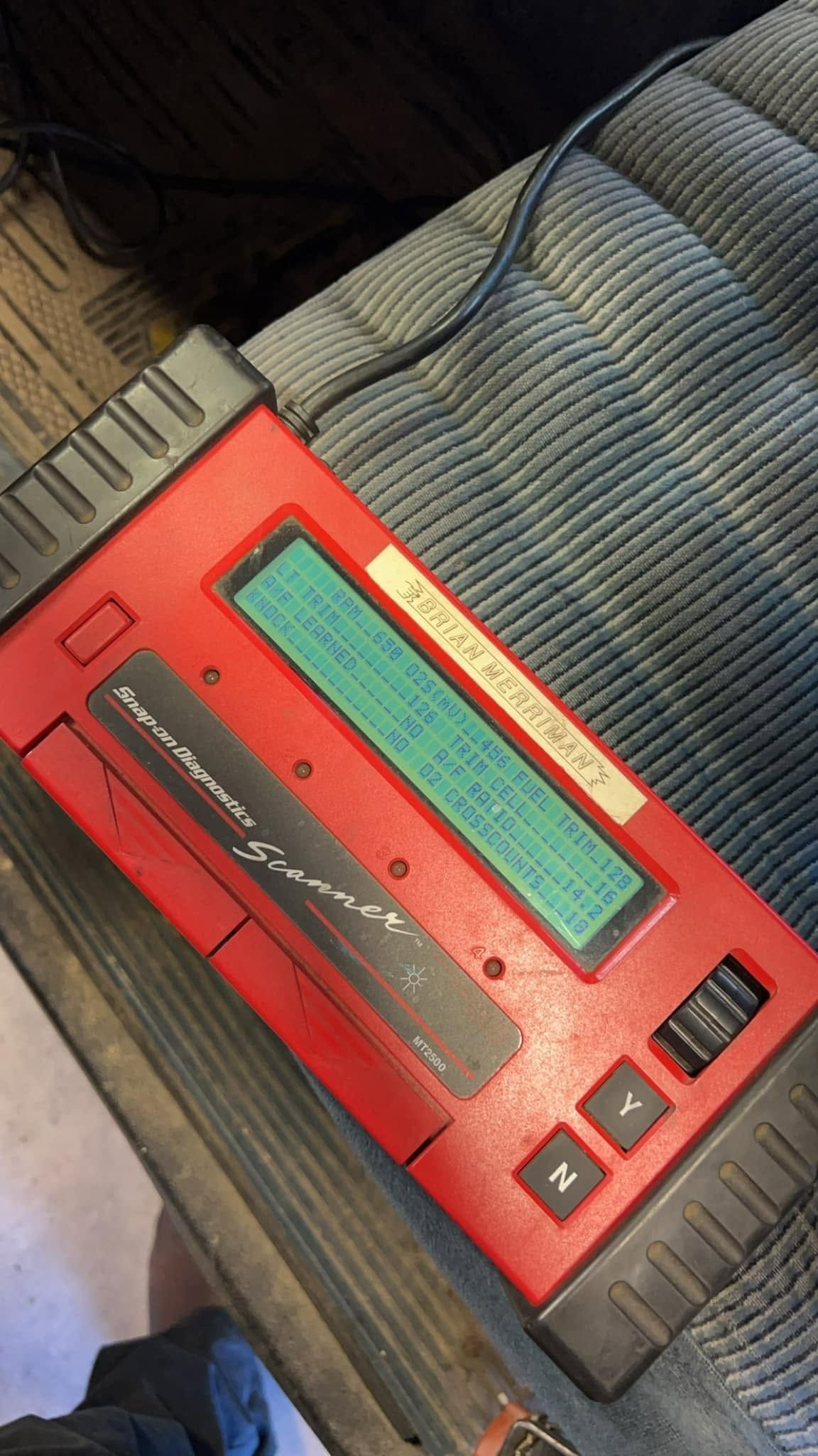 Red handheld electronic device with a screen, buttons, and speaker grilles resting on fabric.