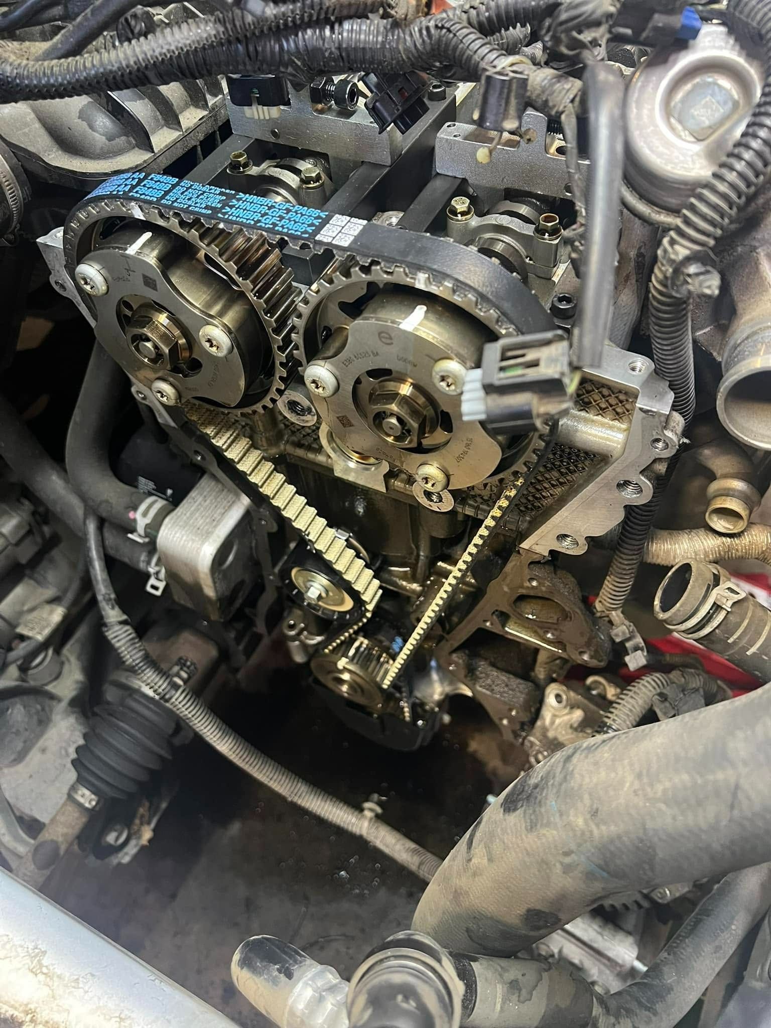 Exposed engine timing components with blue-marked cam gears and chain inside a dusty vehicle engine bay