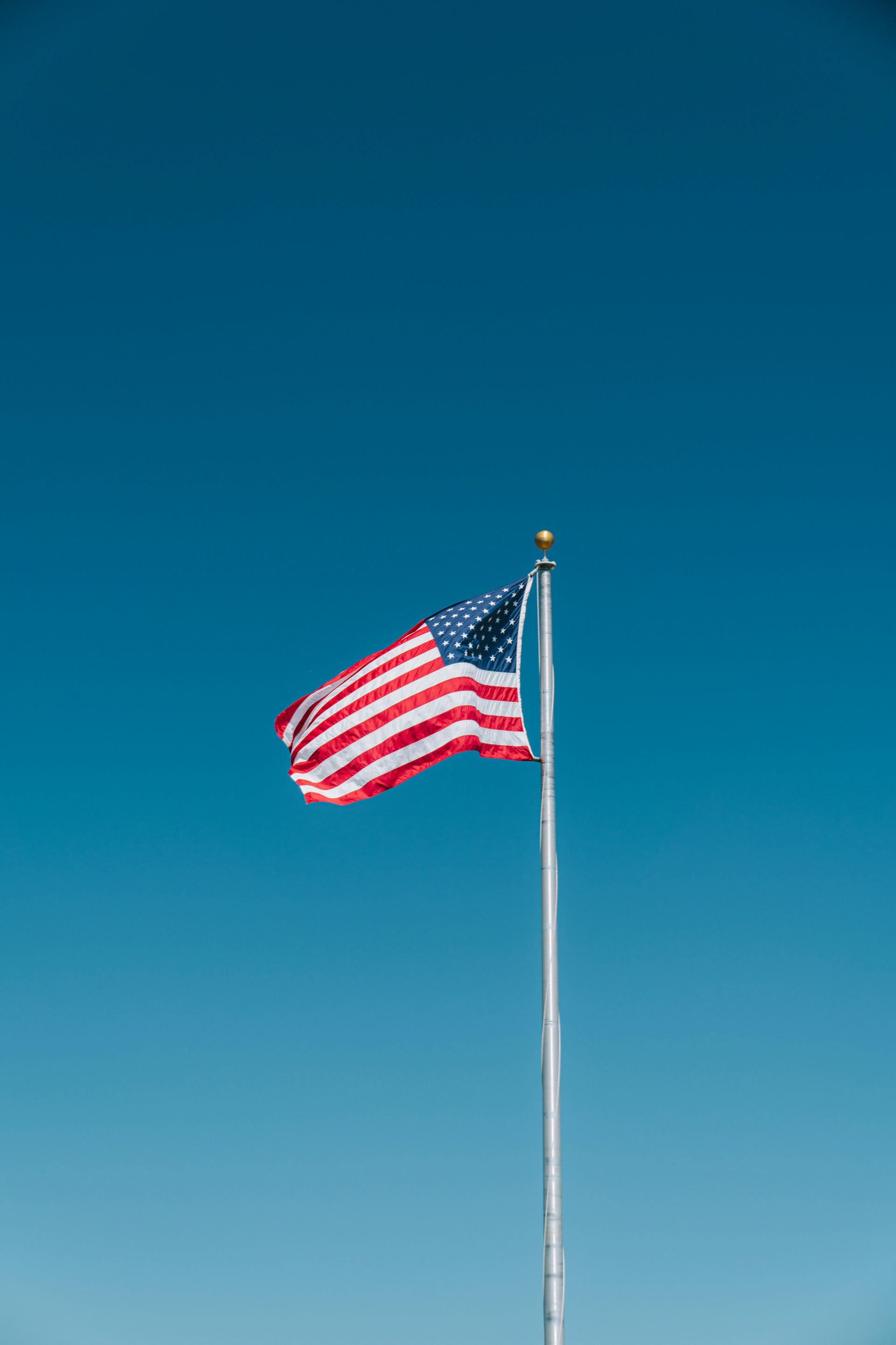 The American flag waving on a tall pole against a clear blue sky.