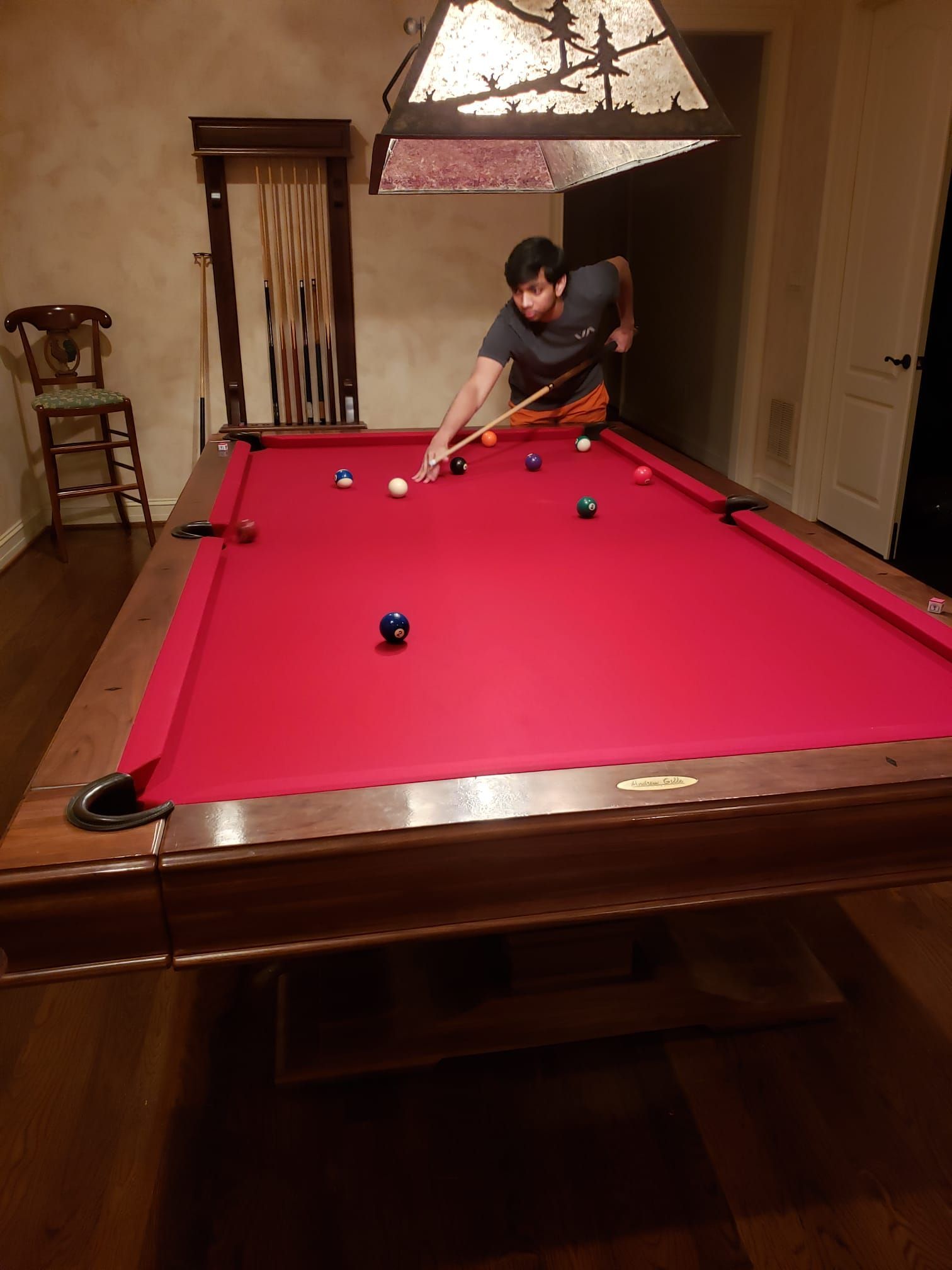 Person lining up a pool shot at a red billiards table in a dim room with a hanging lamp.