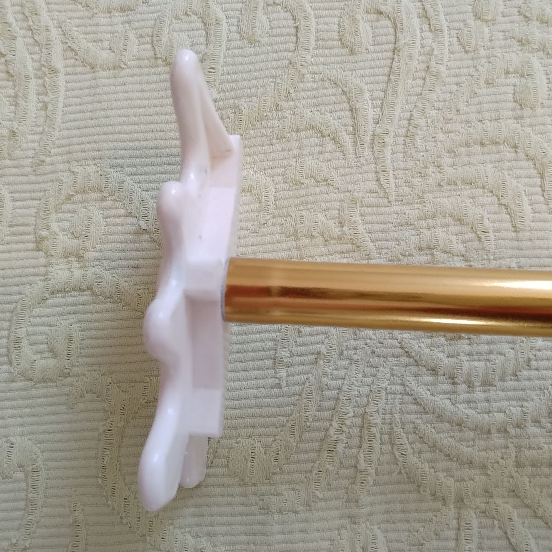 Side view of a white decorative knob attached to a gold-colored rod on a beige textured fabric background