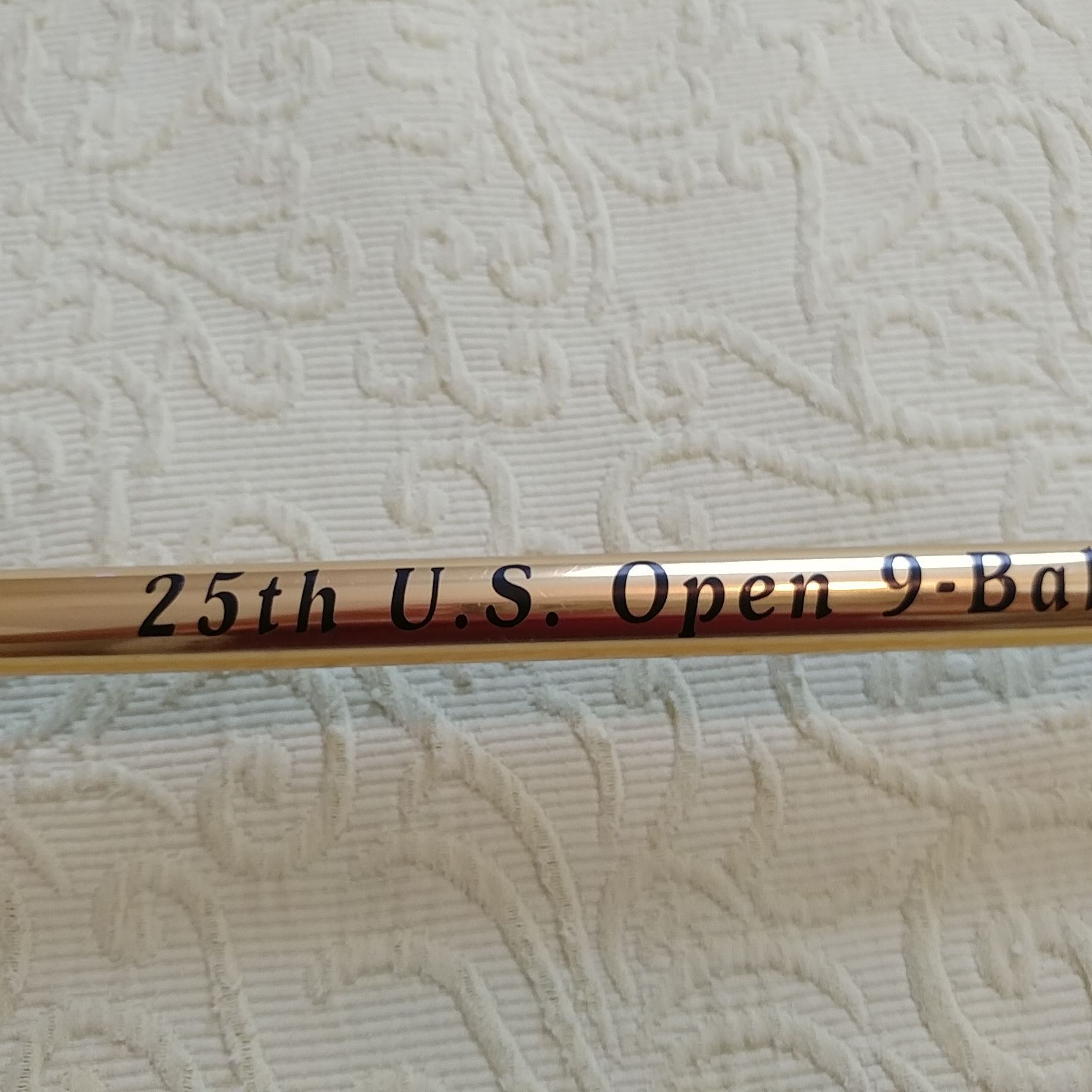 Wooden baseball bat with “25th U.S. Open” text on a textured white fabric background