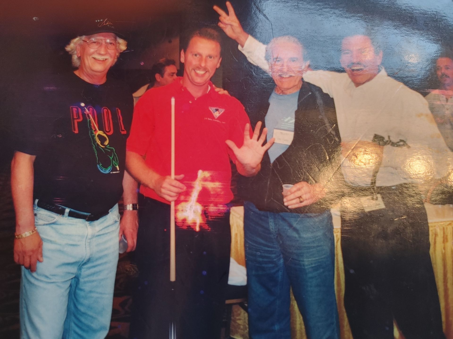 Four people posing indoors, one in a red shirt holding a flare-like light, two smiling and flashing peace signs.