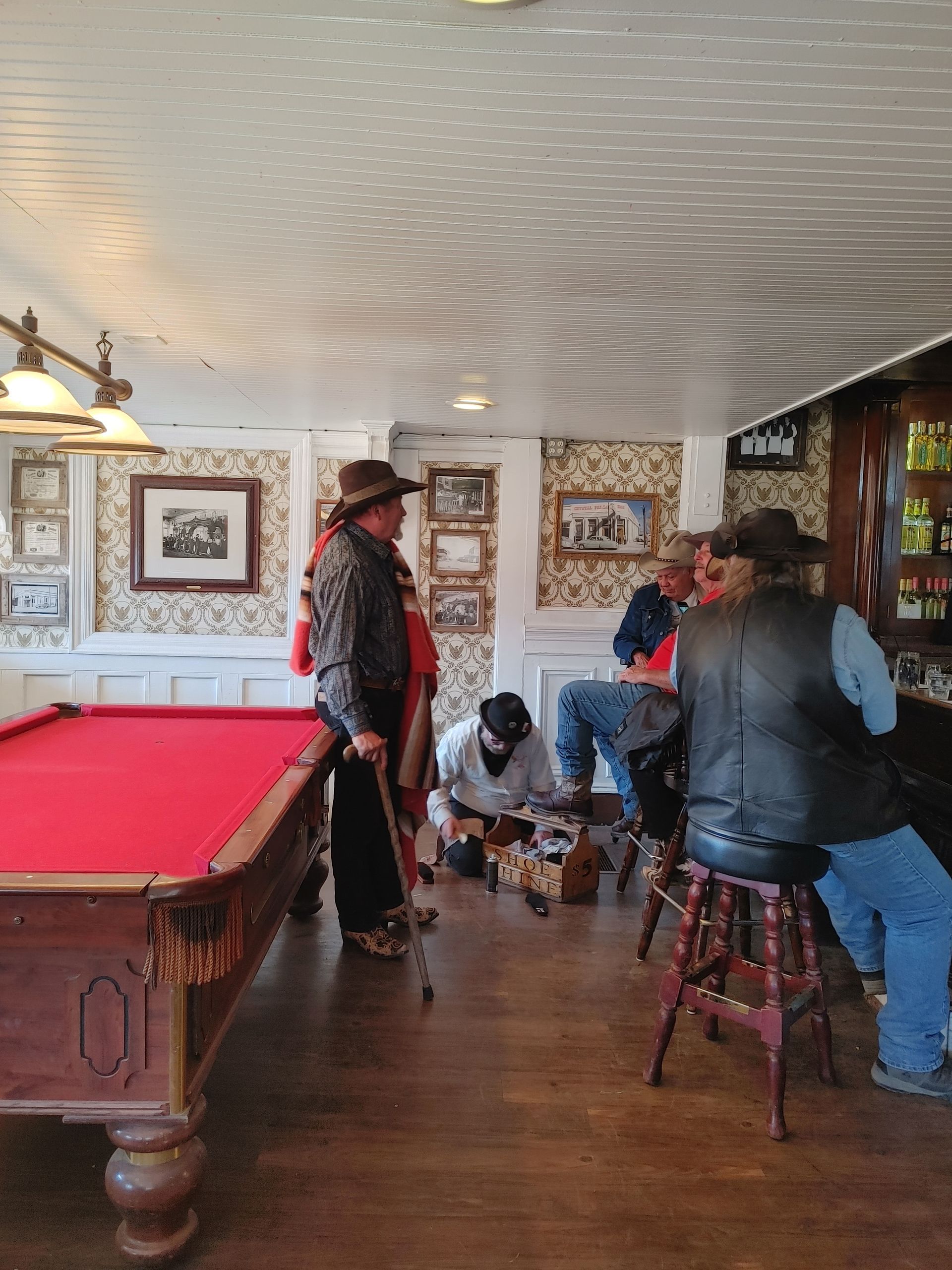 People gathered in a cozy game room with a red pool table and framed art on the walls.