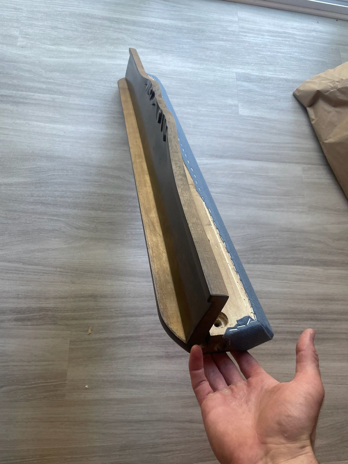 Hand holding a long, damaged cardboard-wrapped object on a wooden floor