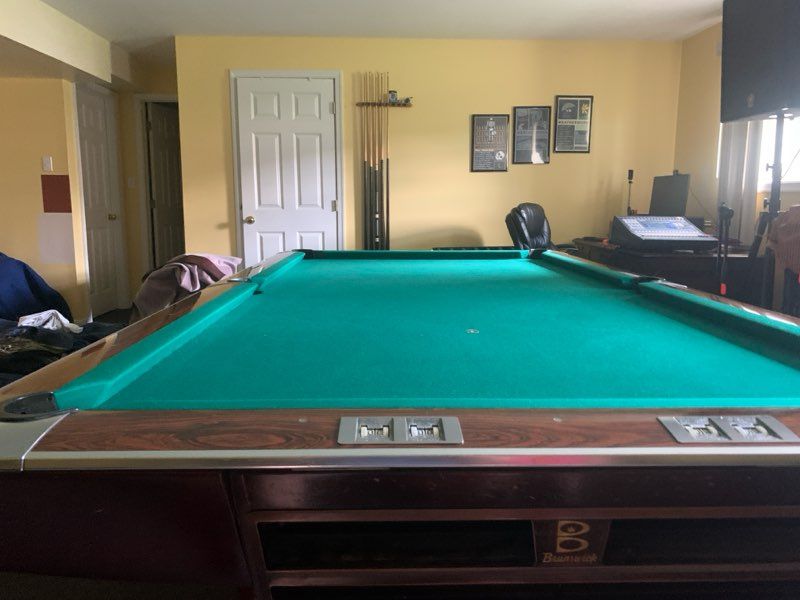 Green pool table in a yellow room with wall art, window blinds, and a chair in the background