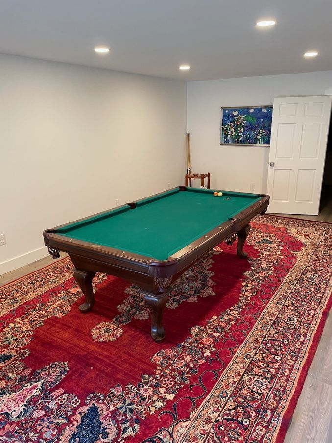 Basement room with a pool table on a red patterned rug and framed art on the wall.