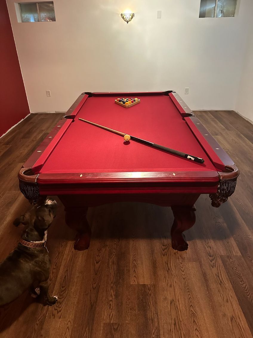 Red-felt billiards table in a room, with a cue laid diagonally across the table.