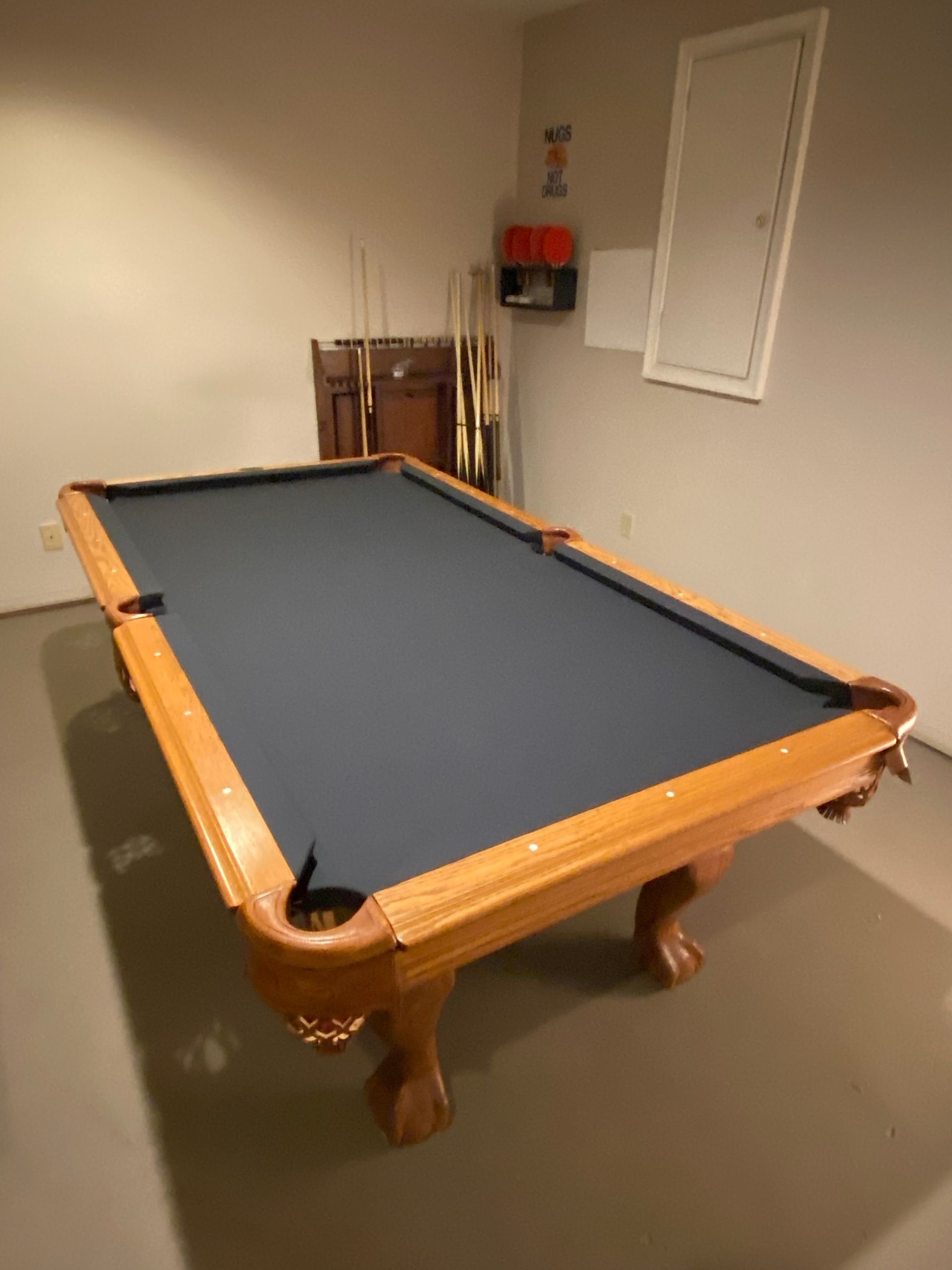 Pool table in a sparse room with beige walls and a small window opening.