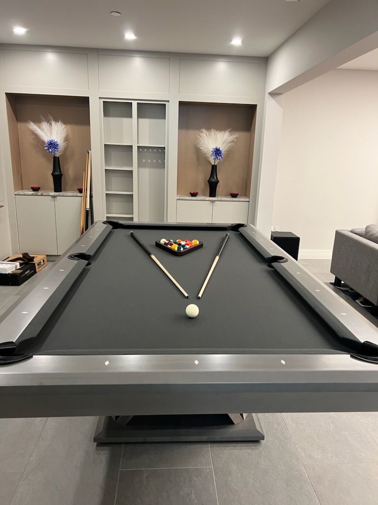Pool table in a modern game room with balls racked at the far end and a cue ball in front.