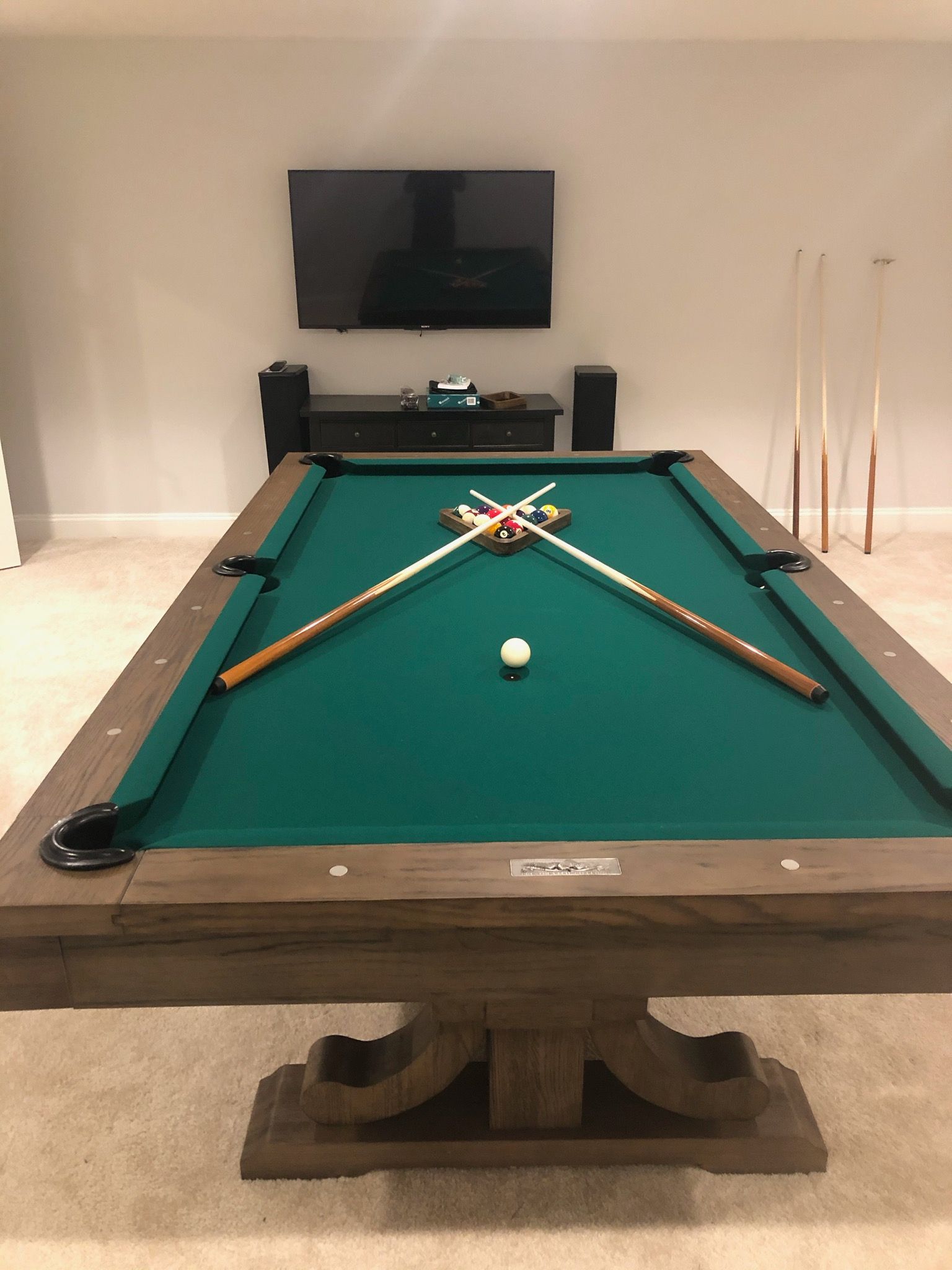 Pool table in a room, with cue sticks crossed over racked balls and a single ball at center.