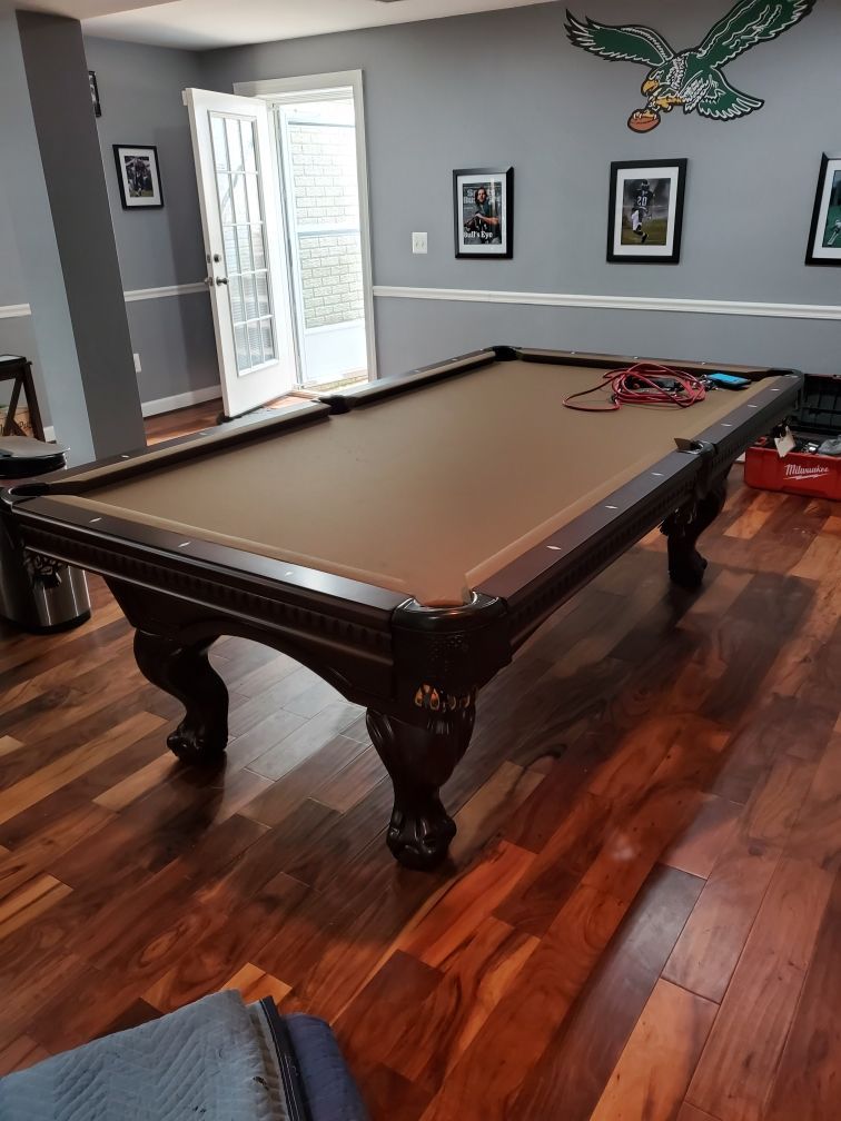 Large brown pool table in a polished hardwood room with gray walls and an eagle wall decoration.