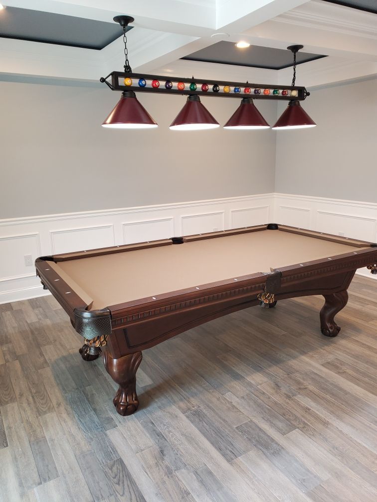 Billiards table in a game room with three hanging red lamps and white-paneled walls.
