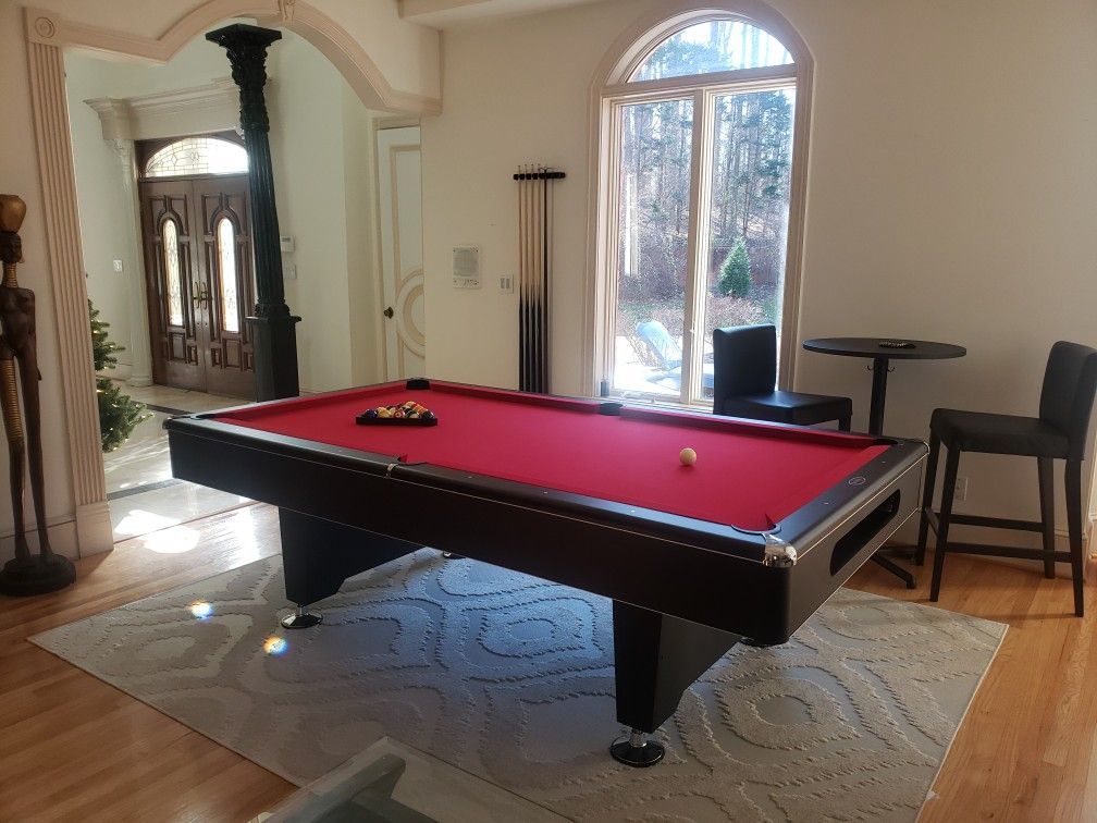 Red billiards table in a bright room with arched windows and a mirrored cabinet.