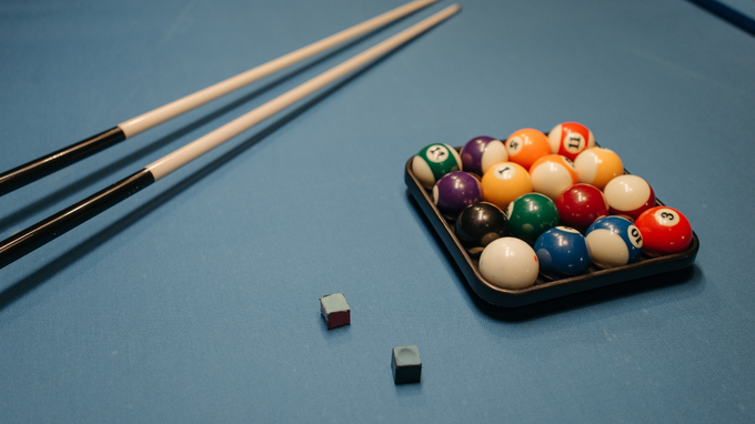 Billiard cues, a rack of colorful pool balls, and two chalk cubes on a blue table