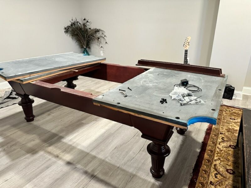 Two billiard tables in a room, one with a torn blue cover and scattered debris.