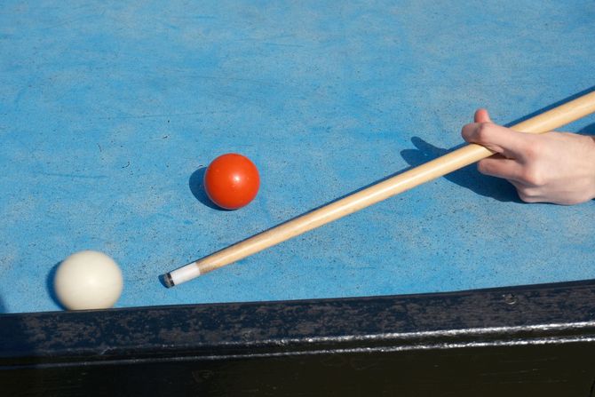 Pool cue aiming at a white ball on a blue billiards table, with an orange ball nearby.