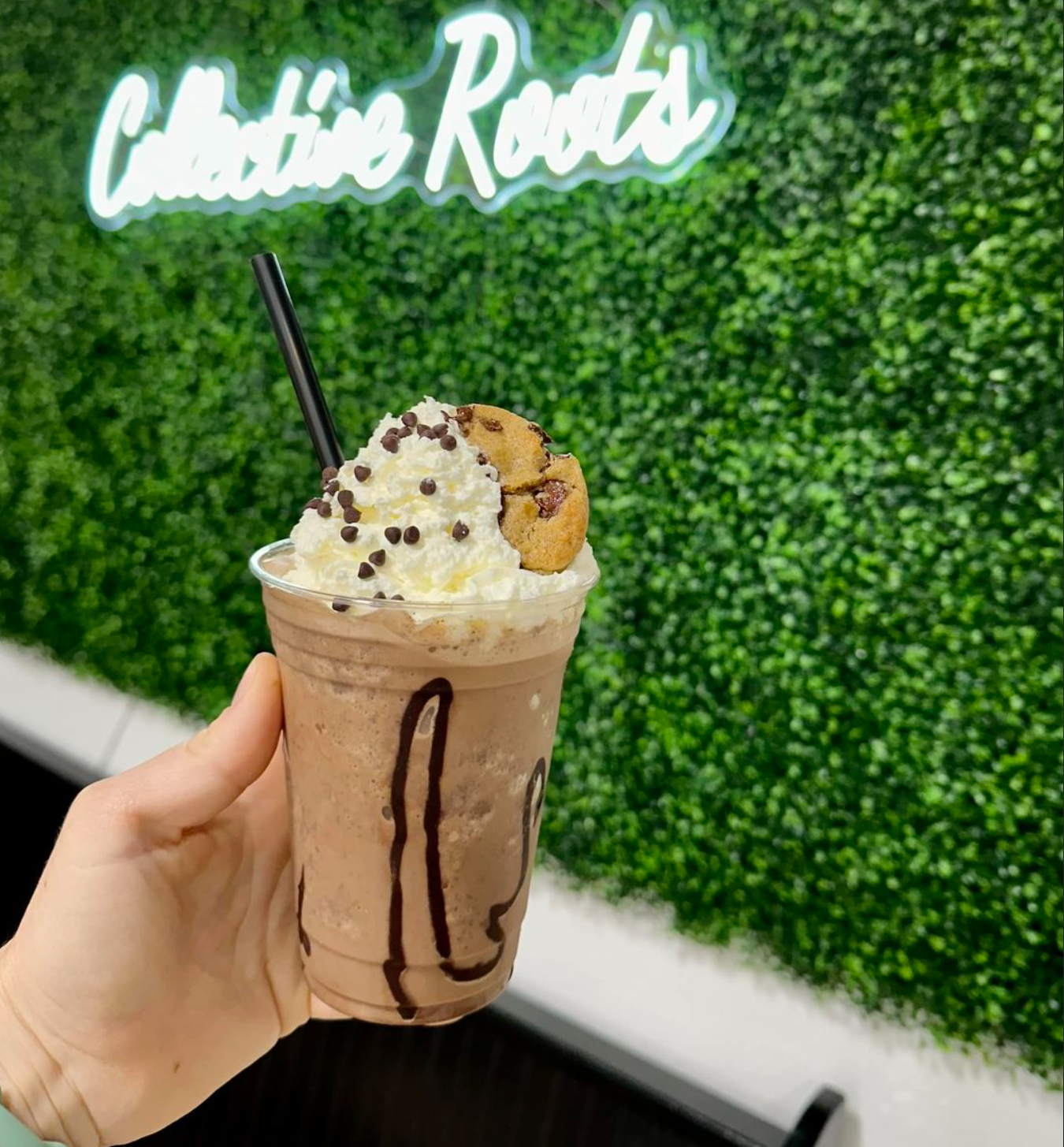 A person is holding a Collective Grounds coffee in front of a sign that says collective roots.