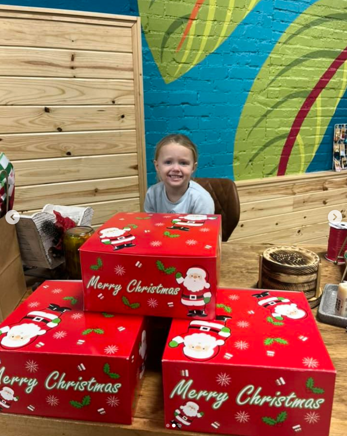 A little girl is sitting in front of a stack of merry christmas boxes.