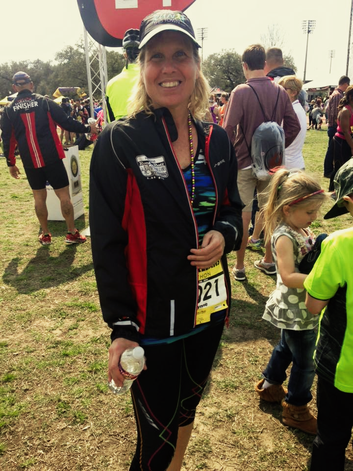Woman in athletic wear at an outdoor event, smiling, holding water bottle, wearing a race bib.