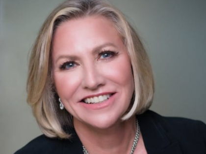 Woman with blonde bob smiles at the camera, wearing a black blazer and silver necklace.