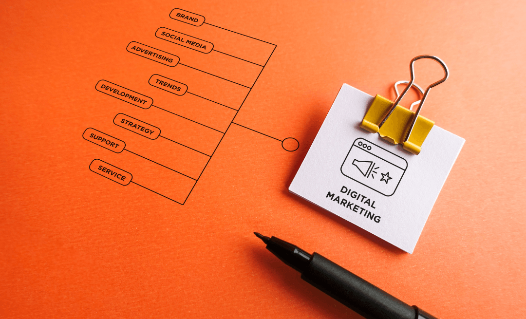 Orange paper with a digital marketing plan graphic, note, and black pen.