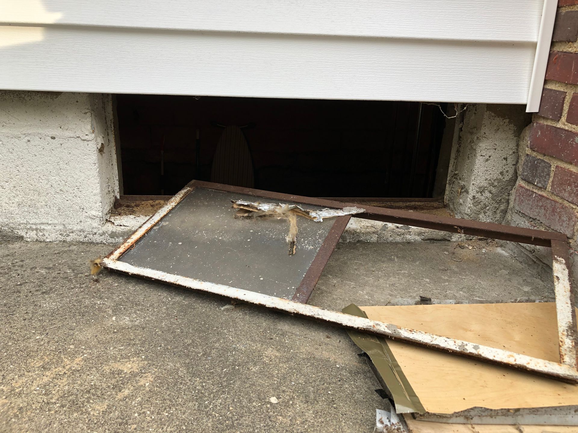 A broken window is sitting on the ground next to a brick wall.