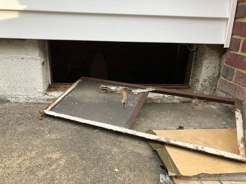 A broken window is sitting on the ground next to a brick wall.