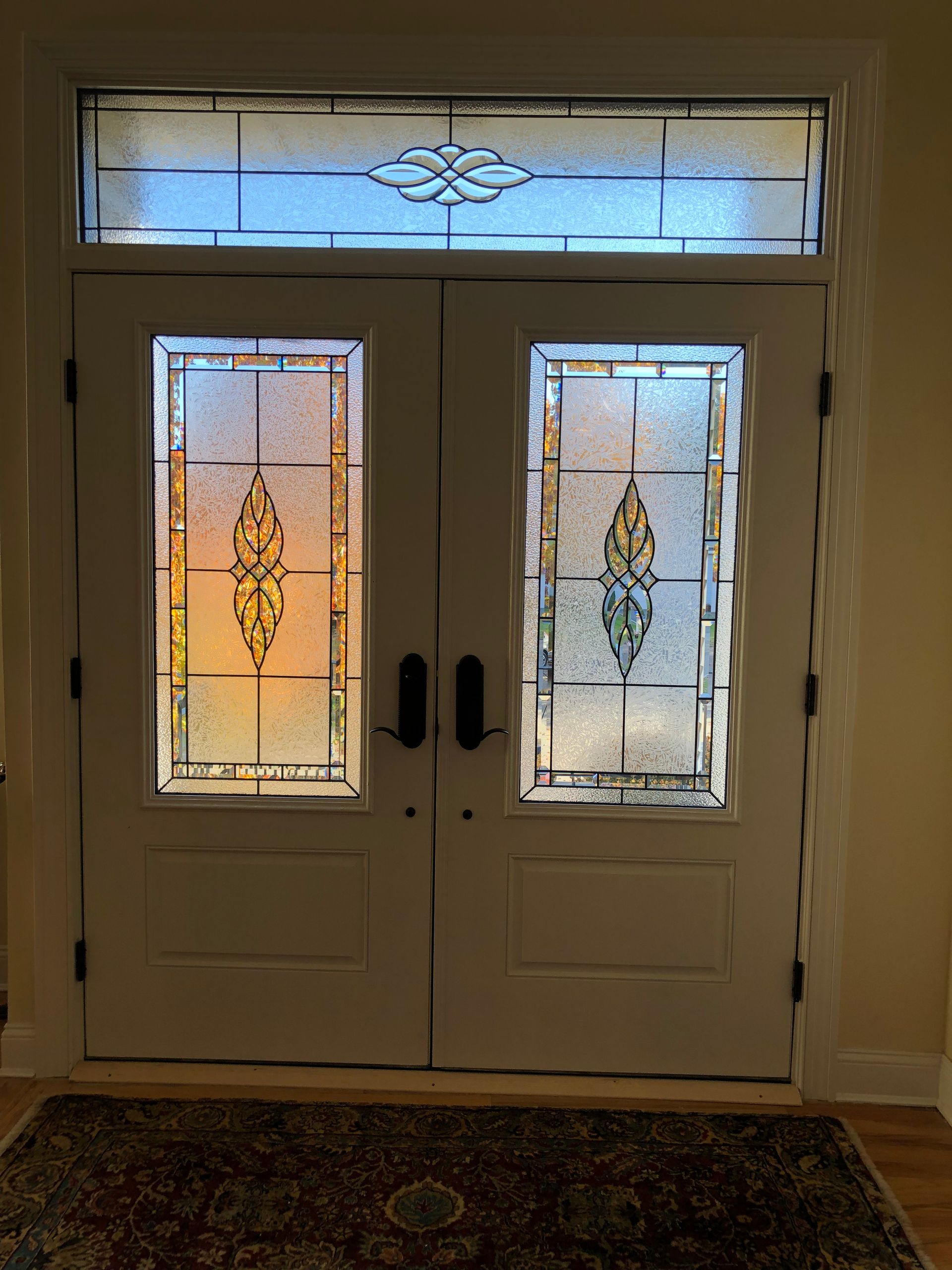 A white door with stained glass windows and a rug in front of it.