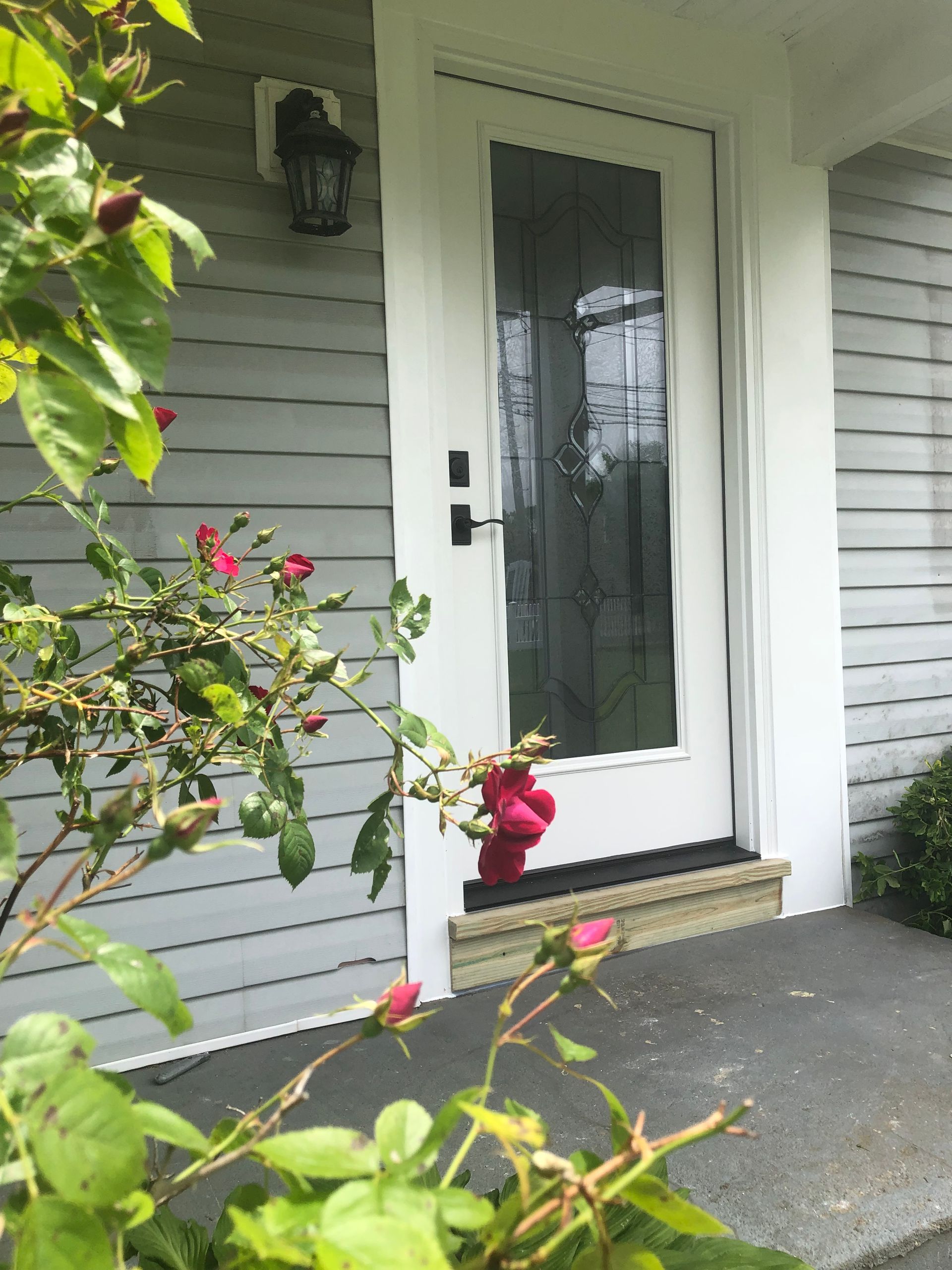 A white door with a glass window is surrounded by flowers on a porch.