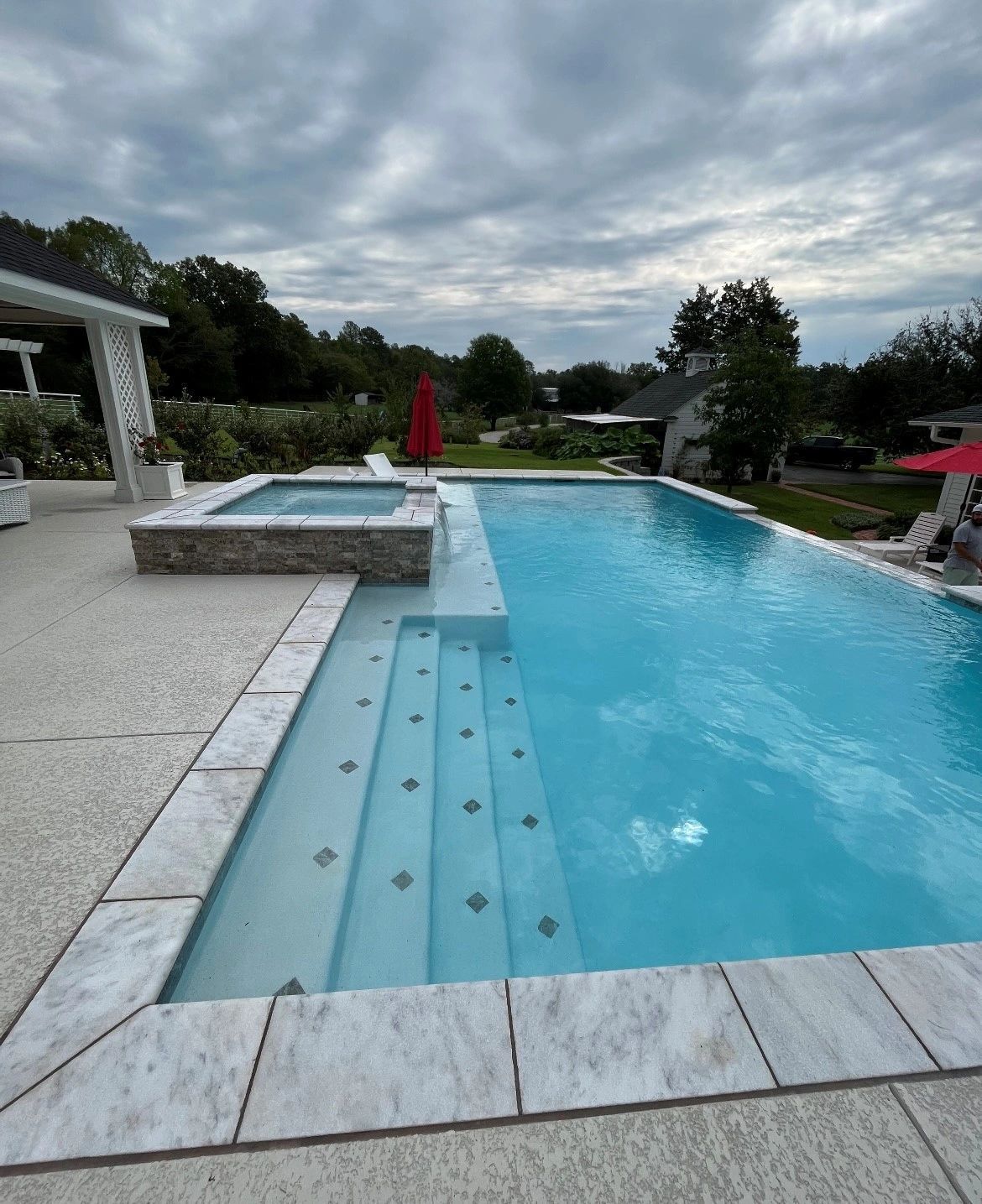 A large swimming pool with stairs and a hot tub in the backyard.