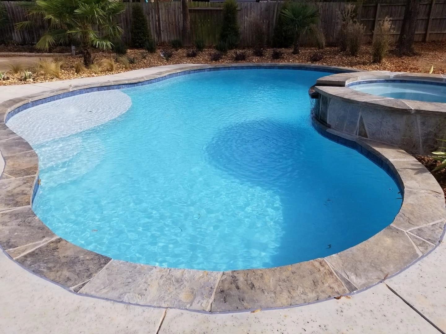 A large swimming pool with a hot tub in the backyard