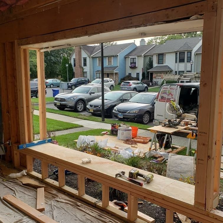 Window frame under construction, looking out at parked cars and houses on a sunny day.