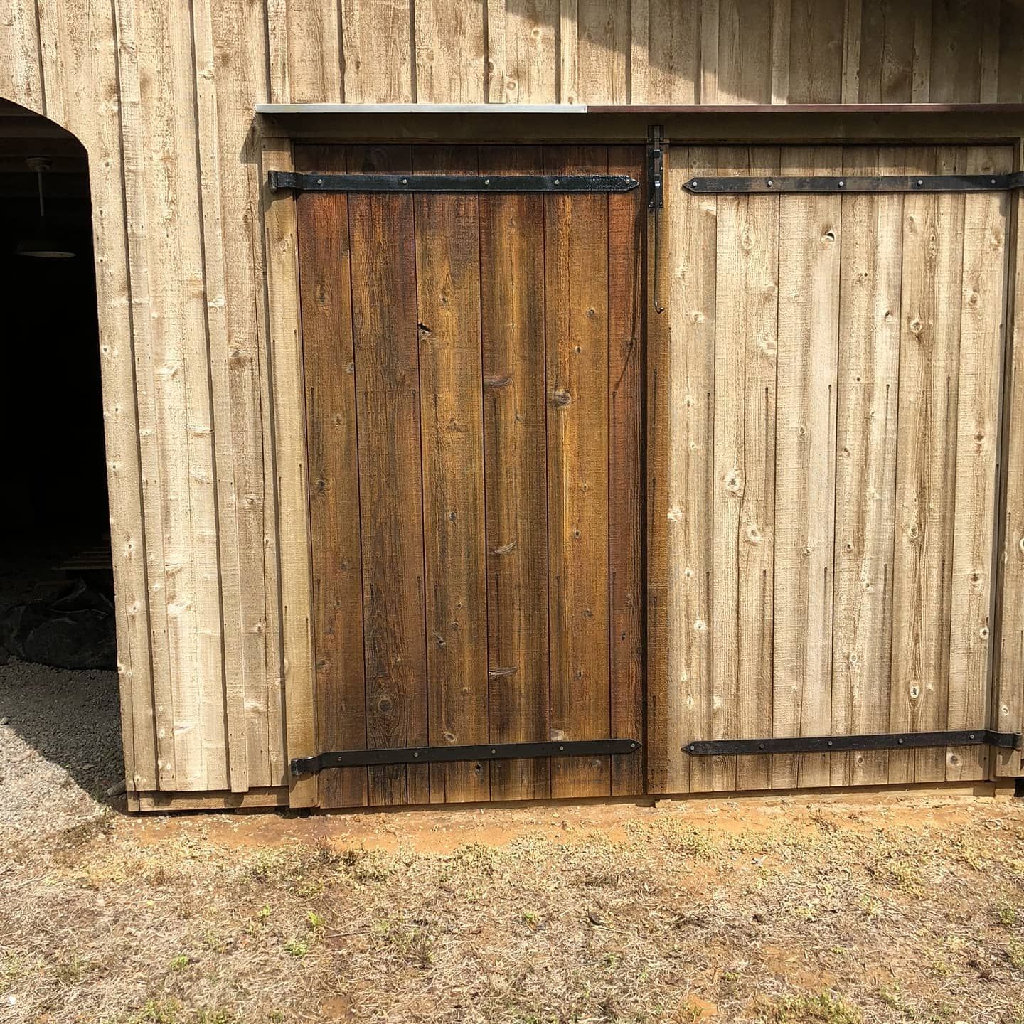 Wooden barn with sliding doors. Dark brown doors, light brown weathered wood walls.