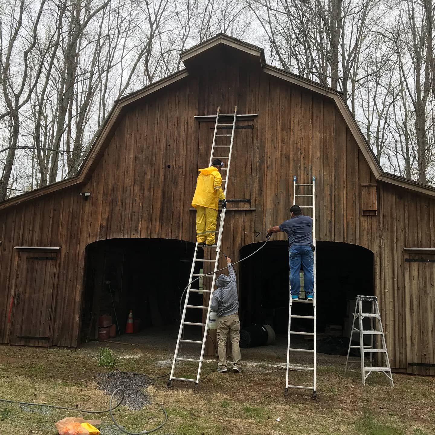 Three people on ladders power washing a wooden barn.