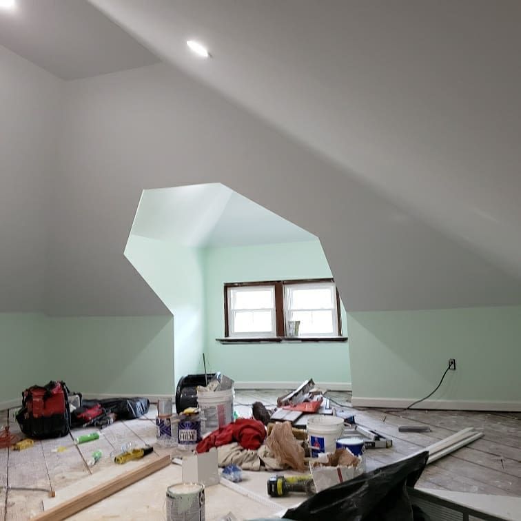 Interior of a room under renovation with tools and paint on the floor, open window in the back.