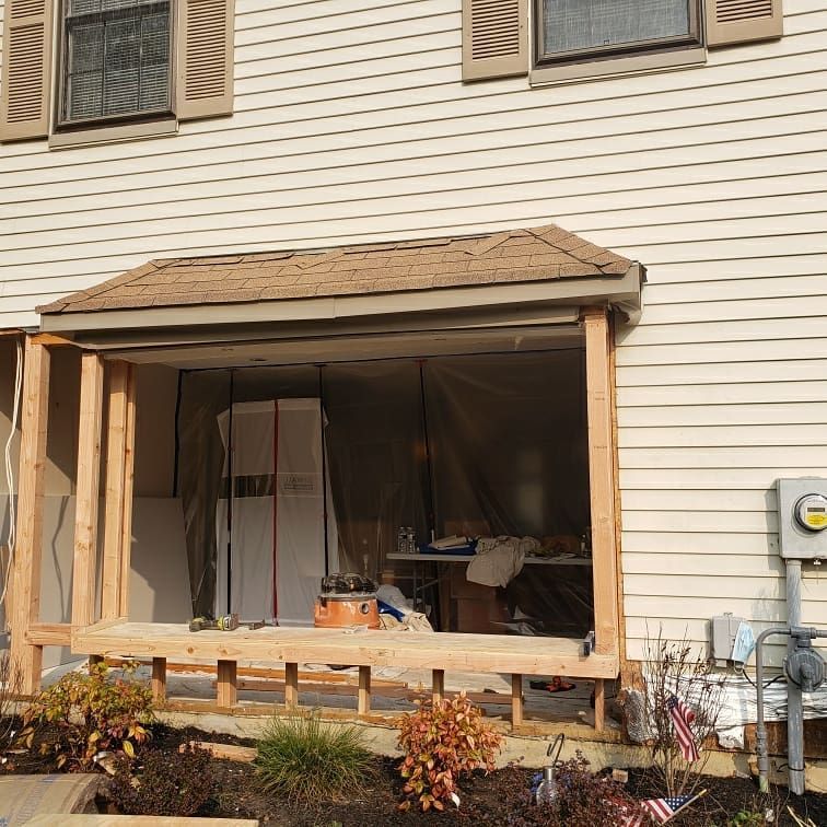 Exterior porch under construction; tan siding, brown roof, wood framing, tarp enclosure.